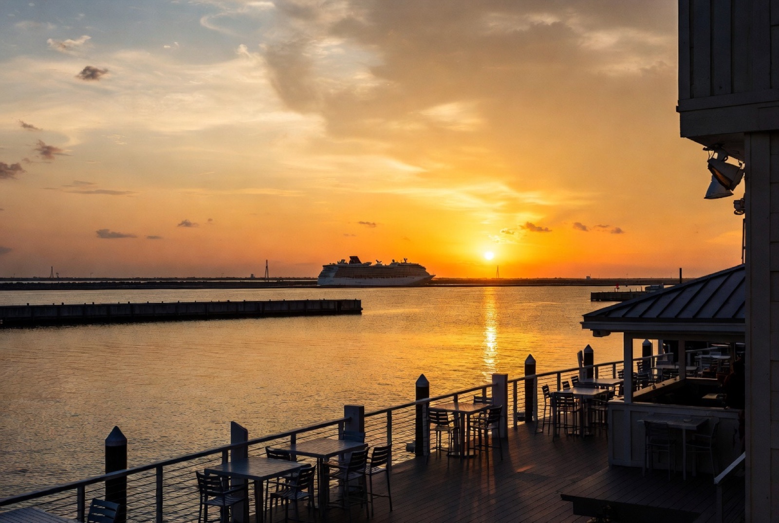 View from a waterfront deck at Port Canaveral at sunset with a cruise ship sailing out in the distance