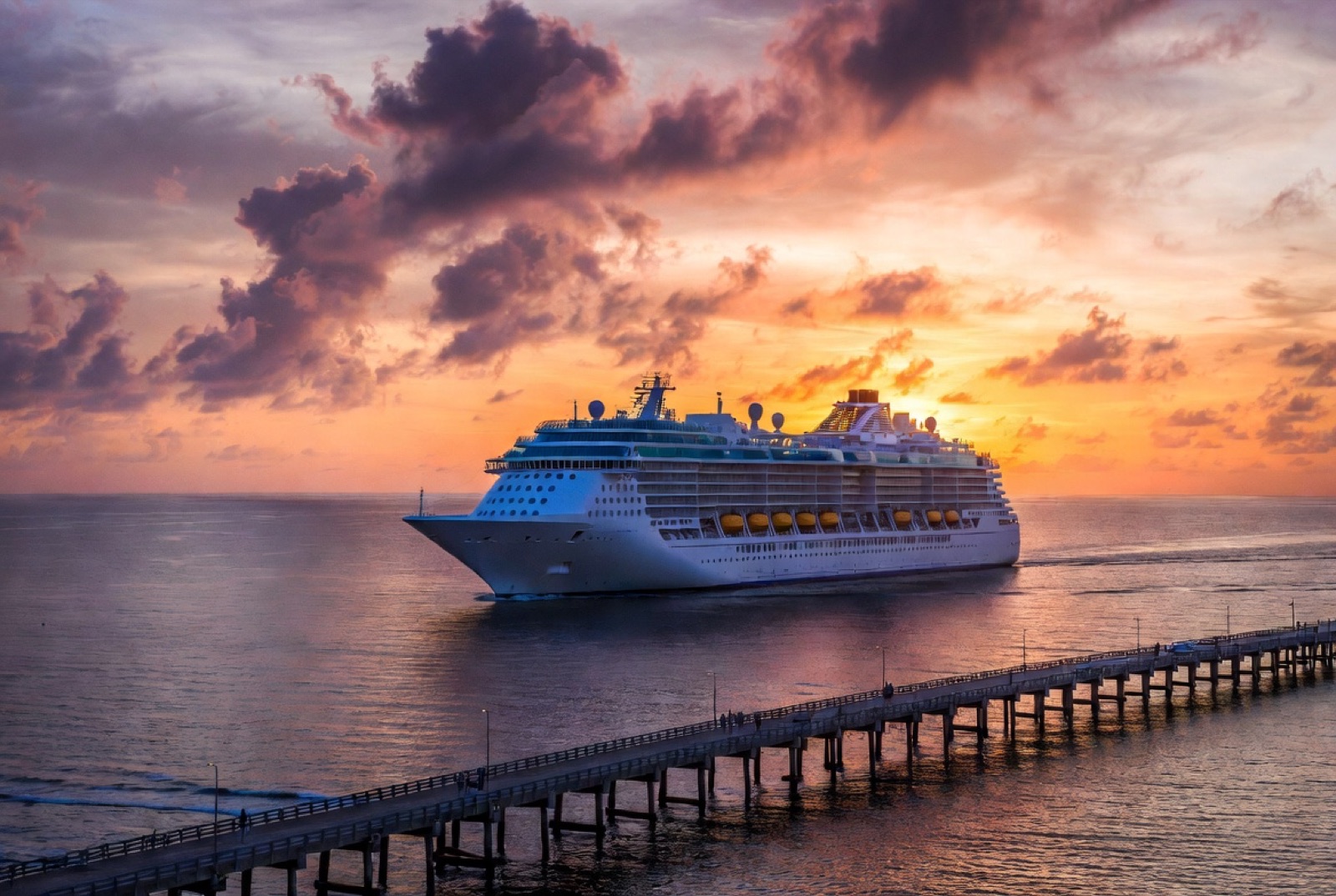 A cruise ship departing Port Canaveral at sunset with the long pier extending into the foreground