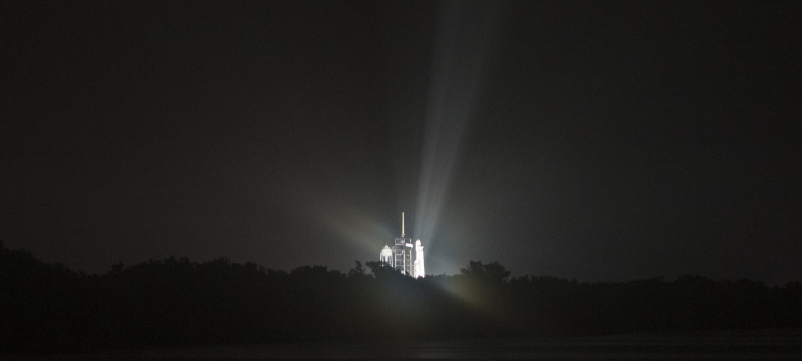 A Falcon Heavy rocket illuminated by floodlights on the launch pad at Kennedy Space Center under a deep night sky