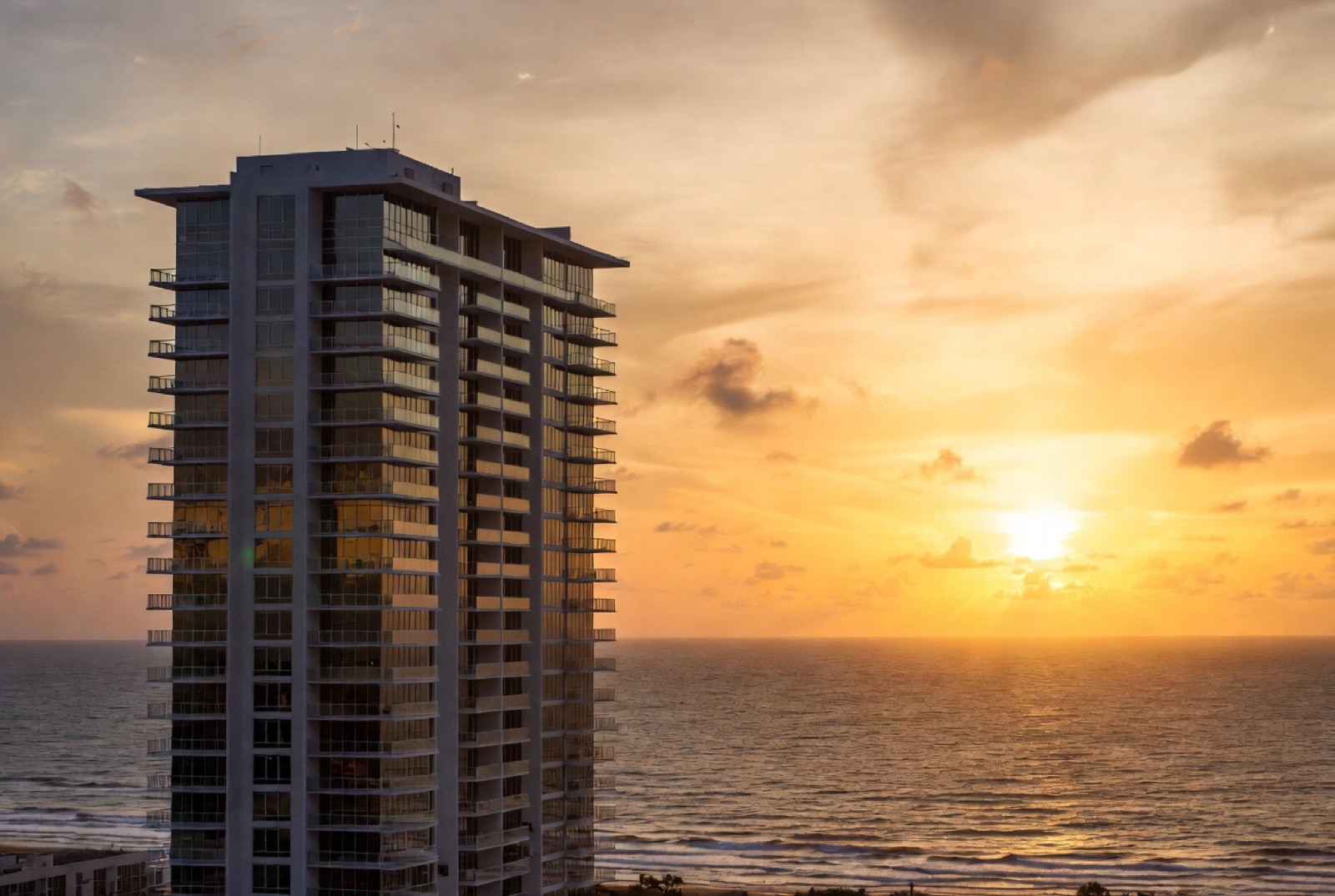 A Cocoa Beach oceanfront condo tower at golden hour with the Atlantic beach below