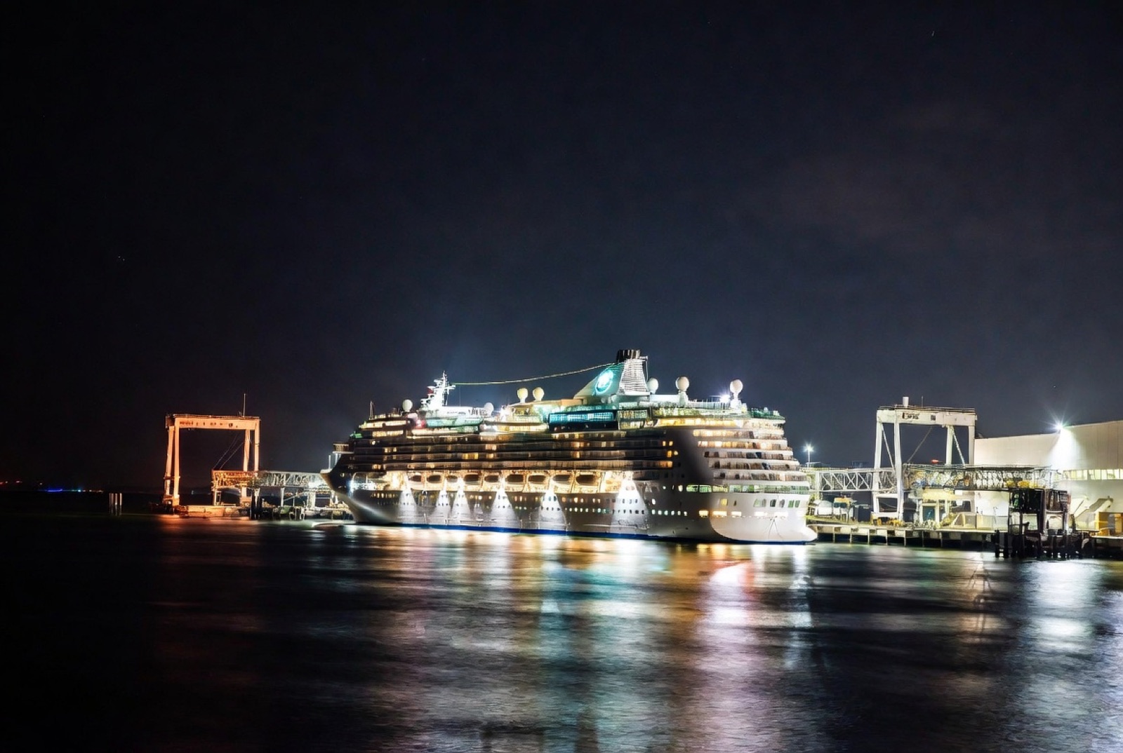 A cruise ship docked at Port Canaveral after dark with terminal lights reflecting on the water