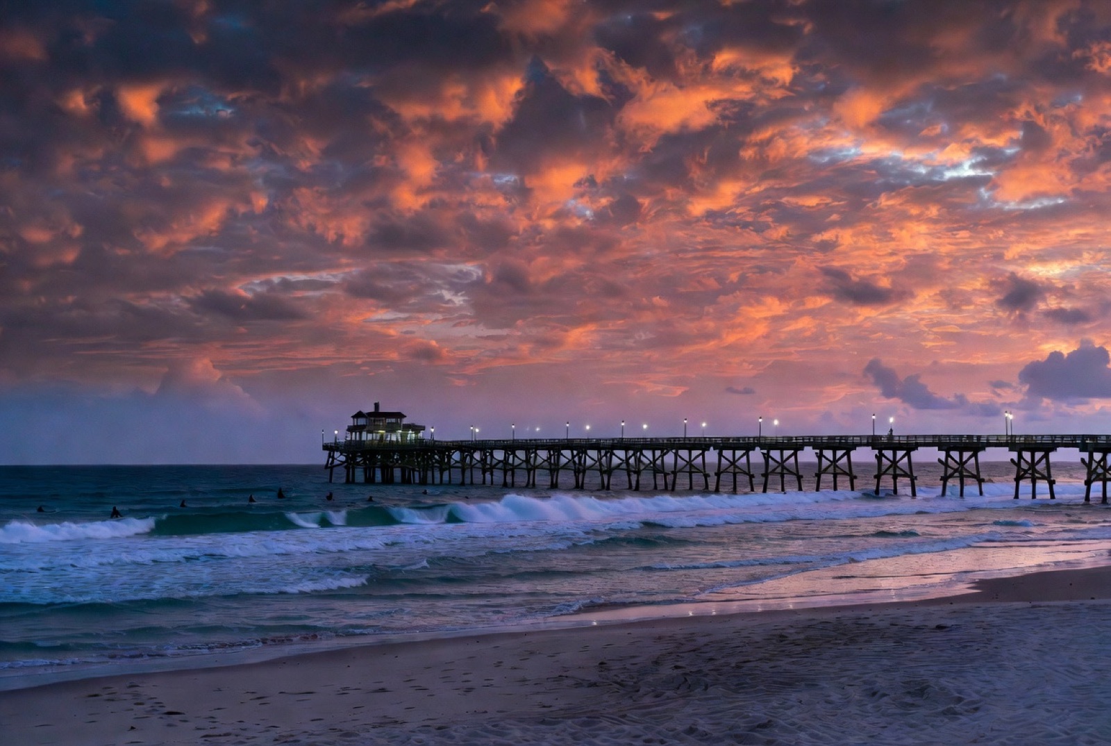 Cocoa Beach Pier extending into the Atlantic at sunset with surfers paddling out below